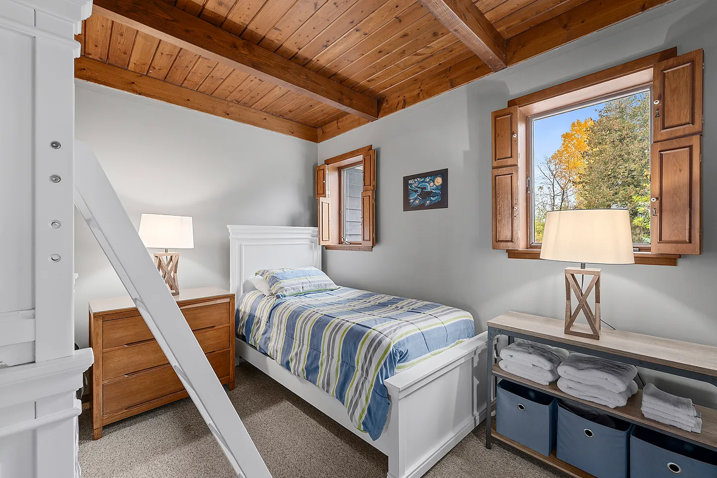 Bedroom with a white single bed, beamed wood ceiling, ladder to a loft, and windows with wooden shutters.