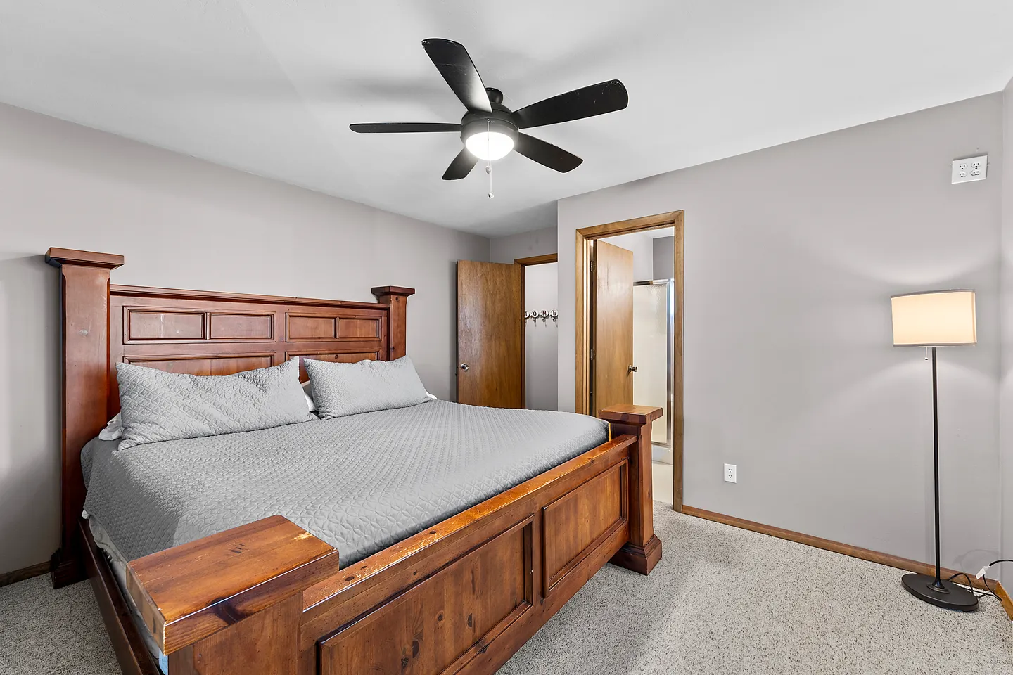 Bedroom with a large wooden bed frame, light grey walls, carpet flooring, a ceiling fan, and open doorways.