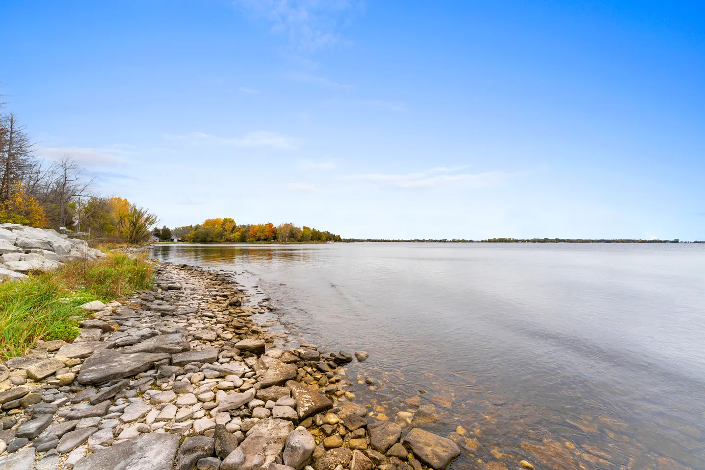 A wide view of a calm lake with a rocky shoreline under a clear blue sky.