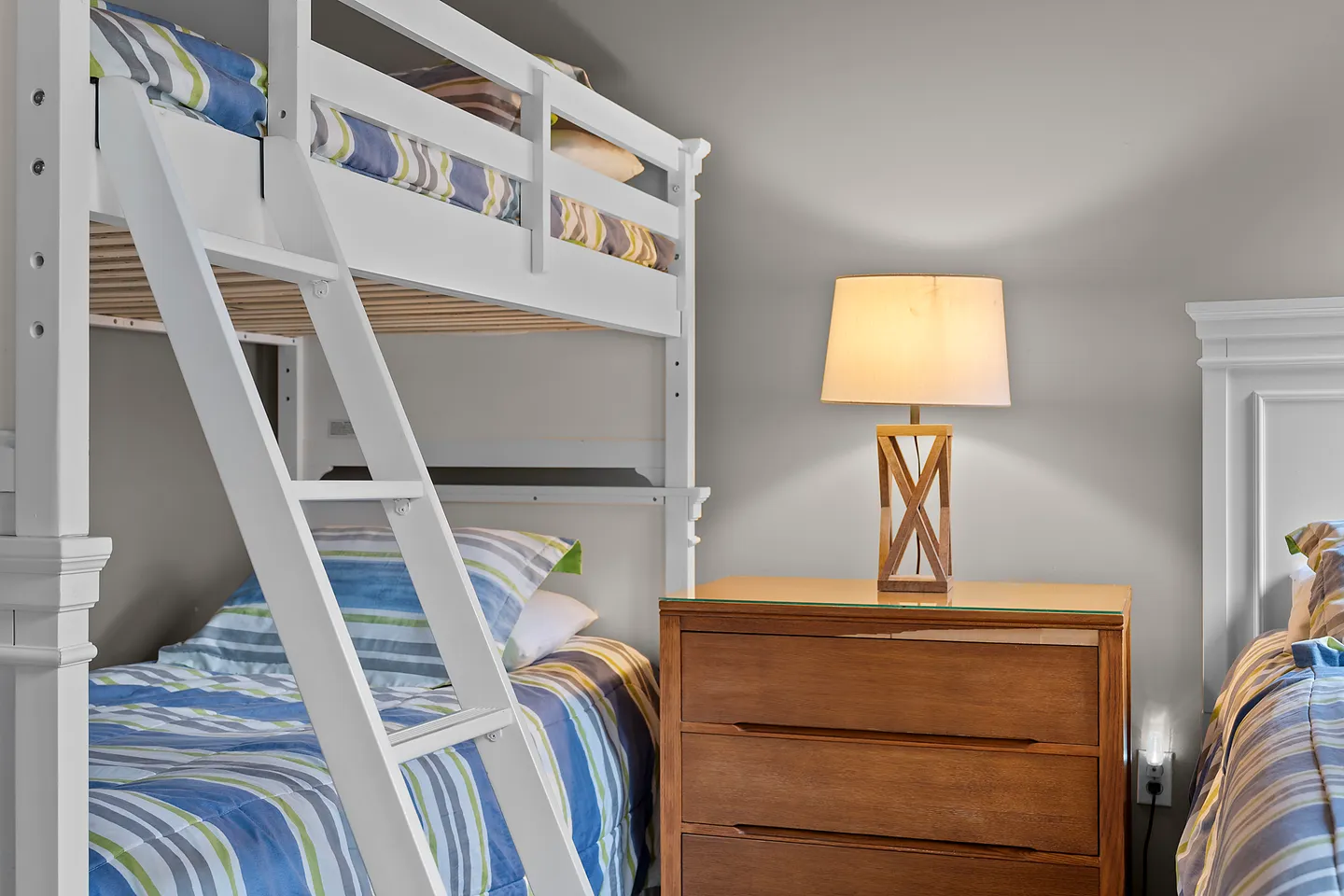 Bedroom featuring a white wooden bunk bed with an attached ladder, a nightstand with a lamp, and an adjacent bed.