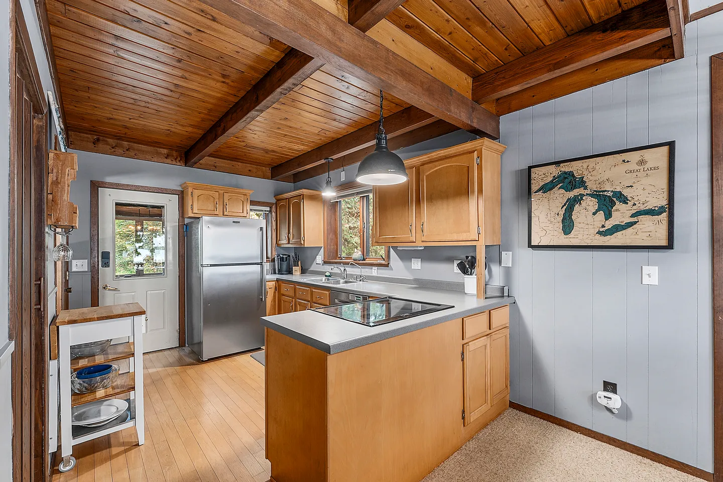 Kitchen with wooden ceiling beams, light wood cabinetry, stainless steel refrigerator, and an exterior door.