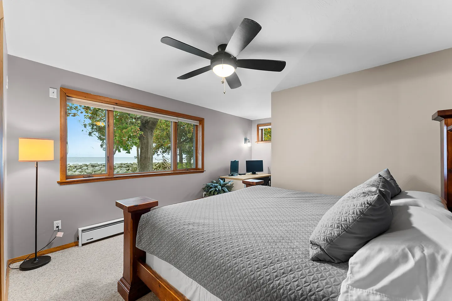 Bedroom with a large bed, ceiling fan, and wide window overlooking a lake and trees.