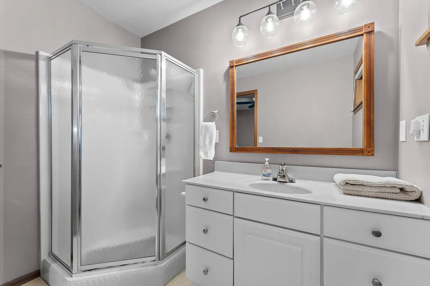 Bathroom with a glass corner shower stall, white vanity sink, and a wood-framed mirror under overhead lights.