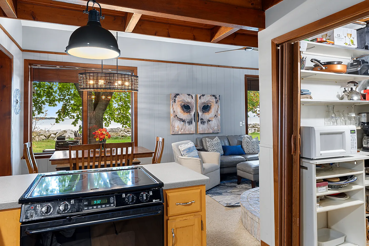 View from kitchen counter showing dining area with large window overlooking water, adjacent living room, and a walk-in pantry on the right.