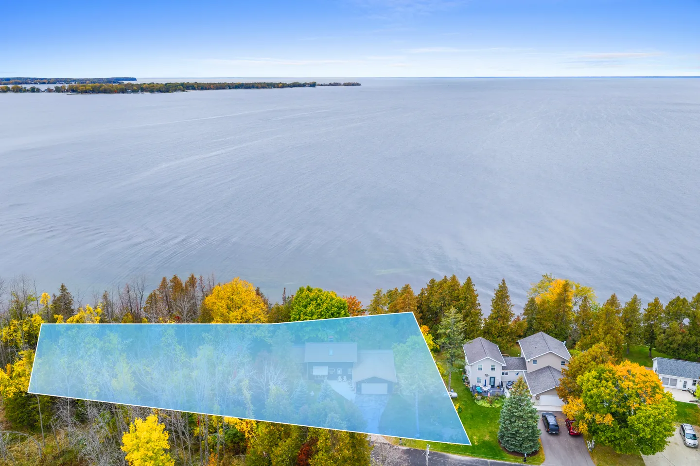 Aerial view of a waterfront property outlined in blue, surrounded by autumn trees along a large body of water.