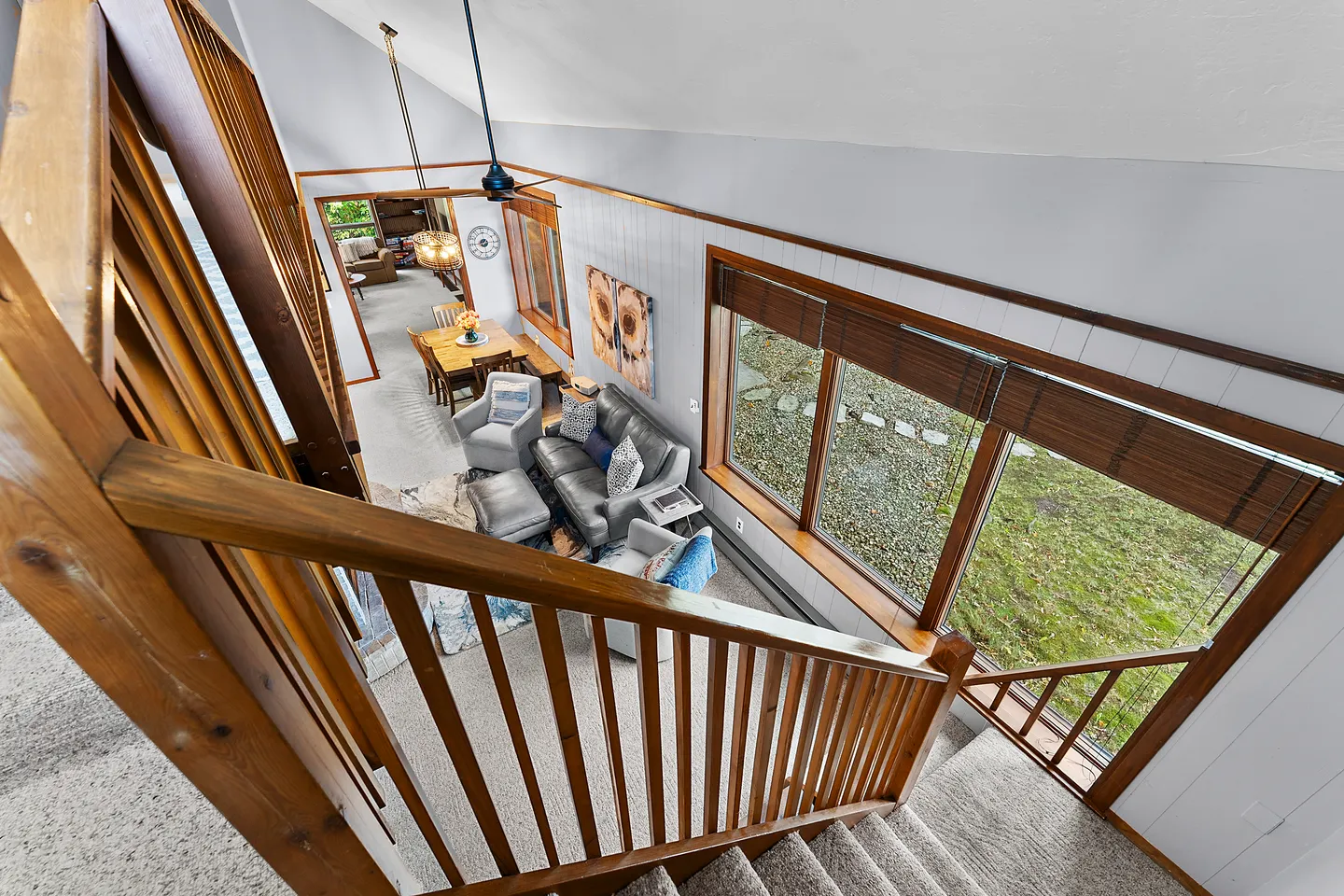 High-angle view looking down a carpeted staircase with wooden railings into a living room with sofas and large windows.