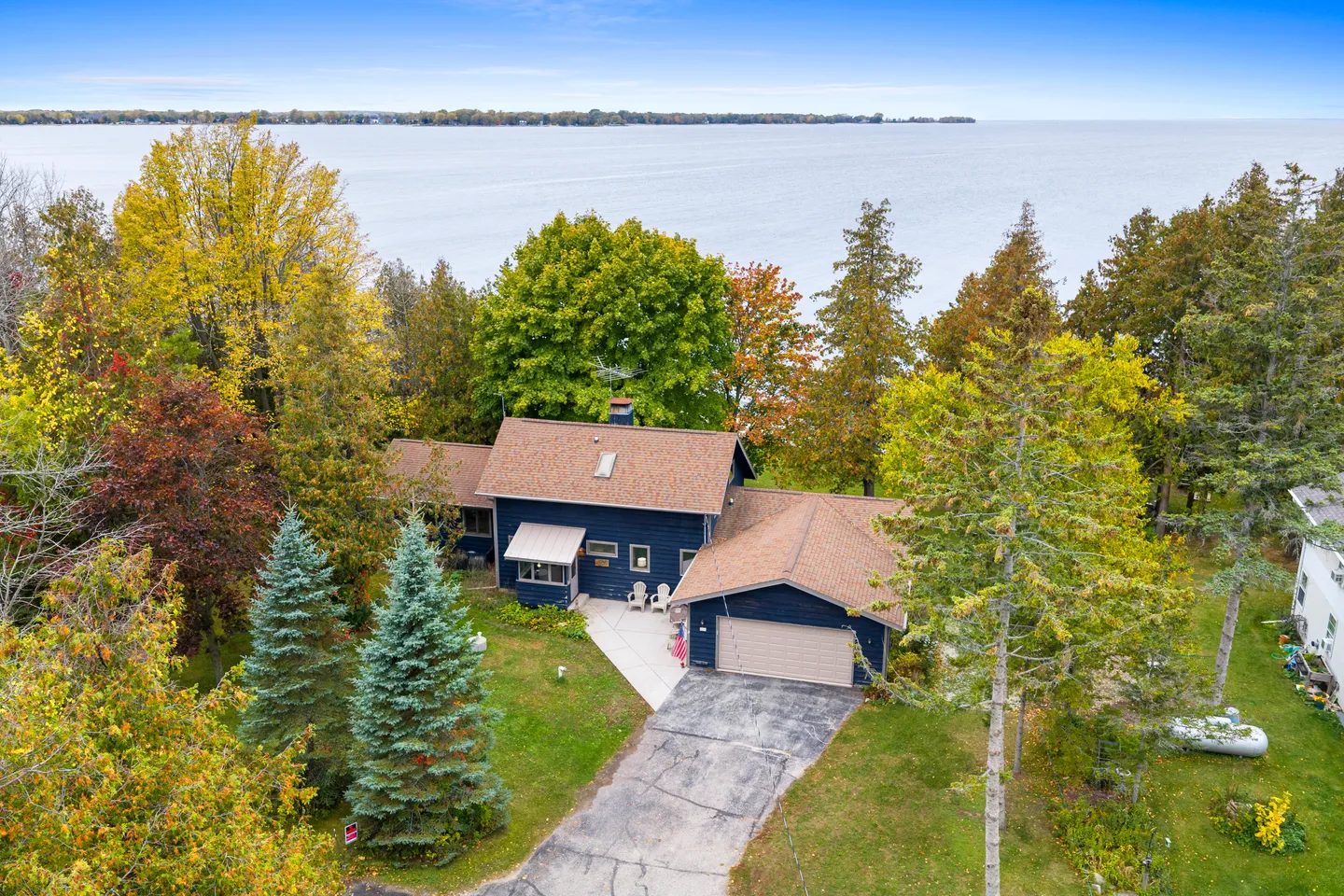 Aerial view of a blue two-story house with an attached garage situated among colorful trees on a lake shoreline.