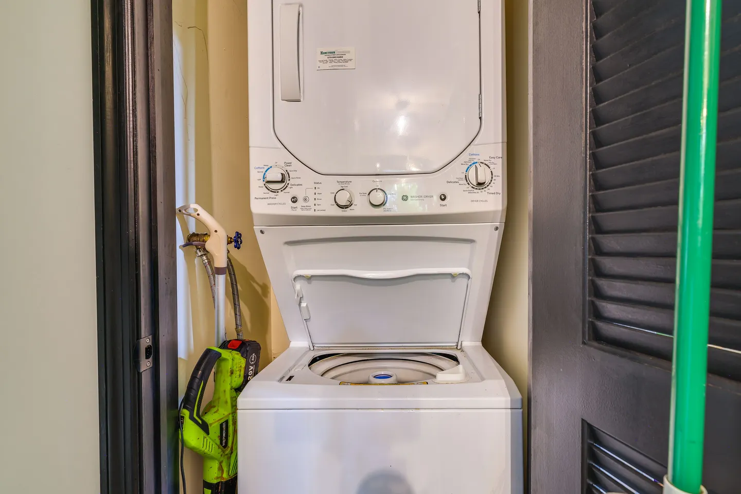A stacked white washer and dryer unit inside a closet with the washer lid open.