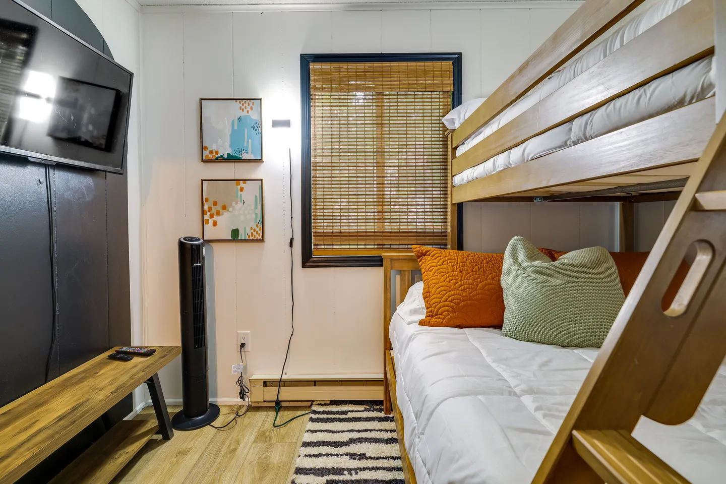 Bedroom featuring a wooden bunk bed, a wall-mounted flat-screen television, a window with woven bamboo shades, and light wood-look flooring.