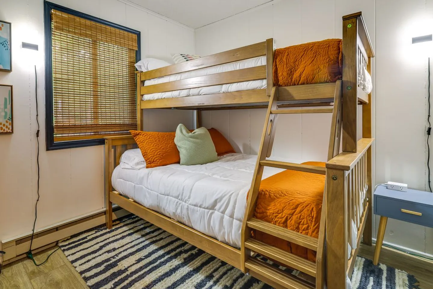 Wooden bunk bed with white and orange bedding next to a window with bamboo blinds in a bedroom.