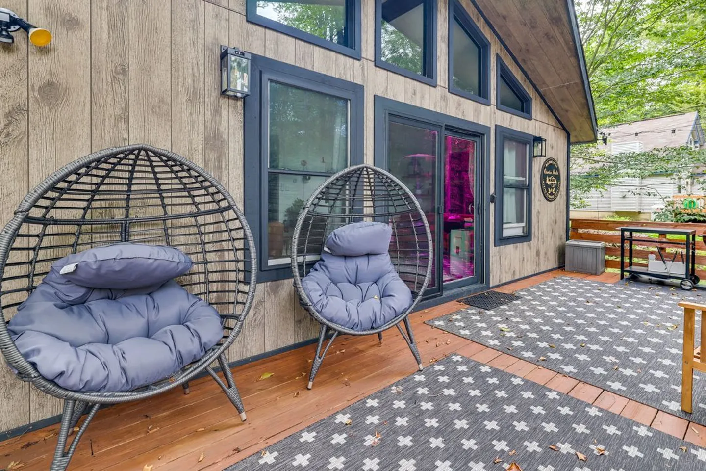 Outdoor deck with patterned rugs, two spherical pod chairs with cushions, and sliding glass door entrance.