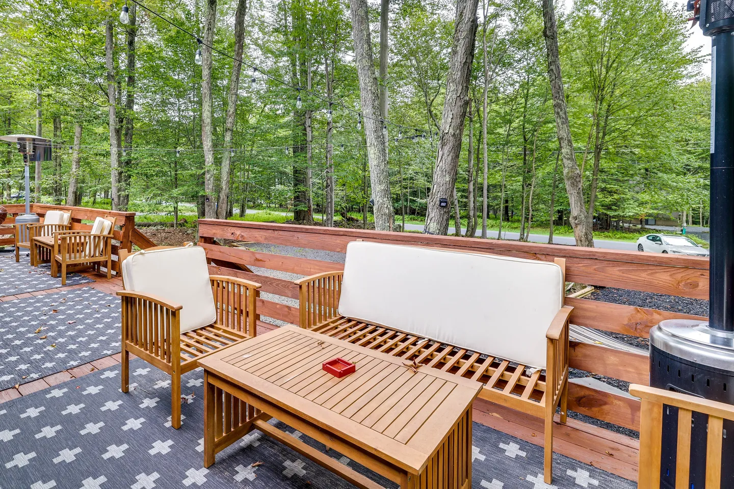 Outdoor wooden deck with slatted wood patio furniture, an outdoor rug, patio heaters, and a wooded forest view.