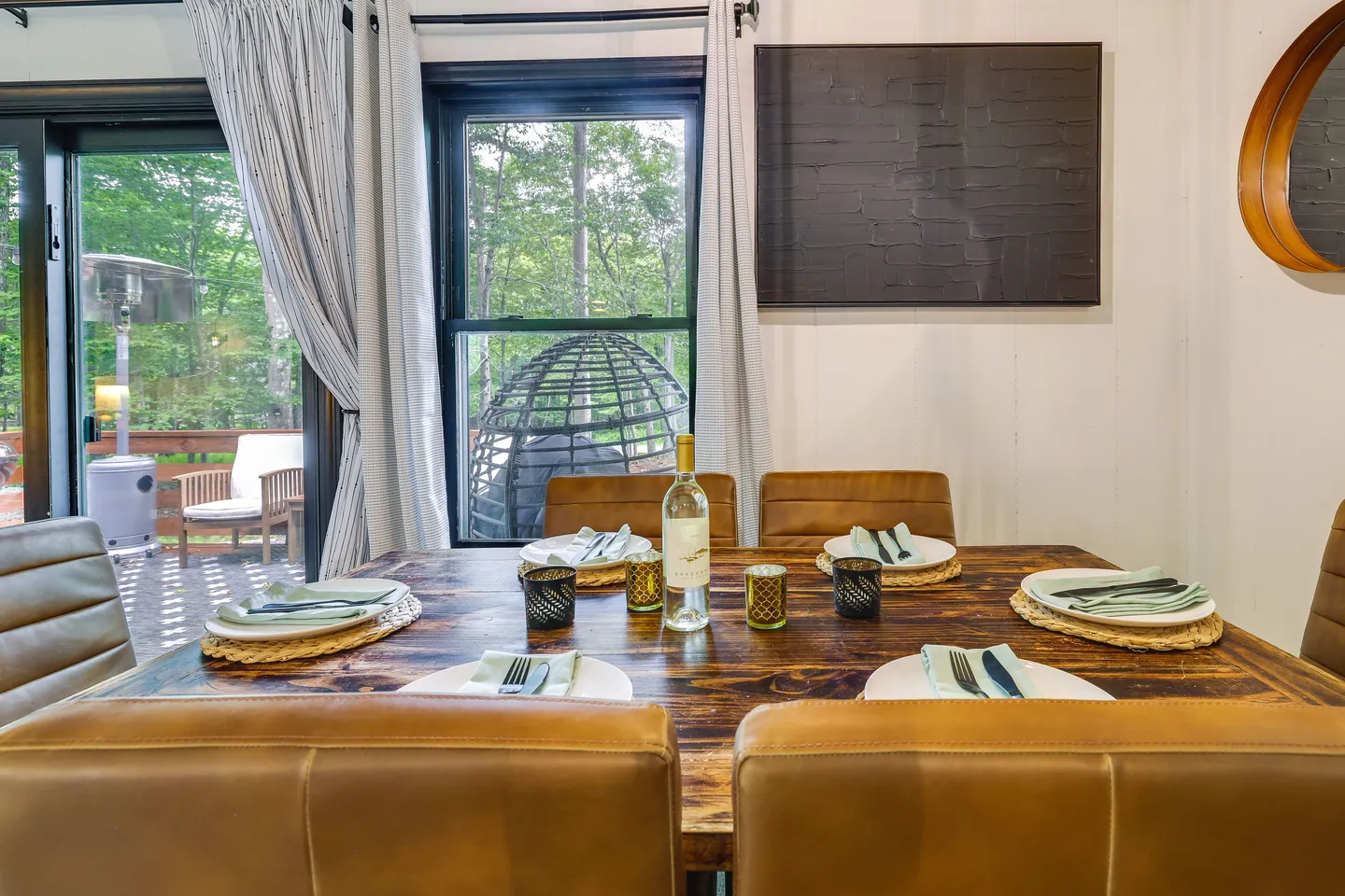 Dining table set with plates, silverware, and wine, surrounded by brown leather chairs in front of a window overlooking a deck.