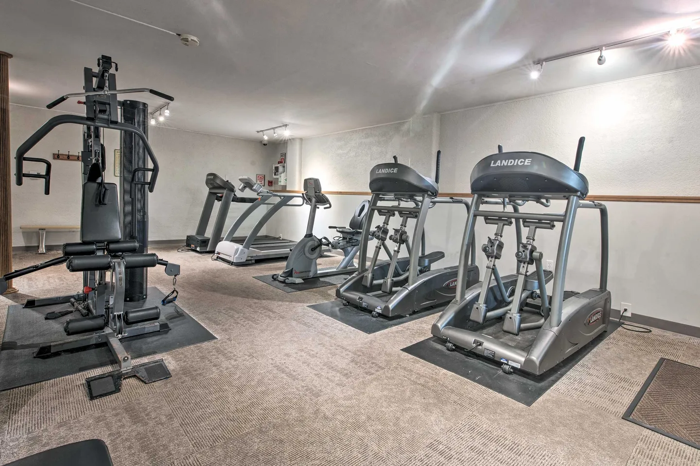 Indoor fitness room with treadmills, elliptical machines, a stationary bike, and a multi-station weight machine on carpeted flooring.