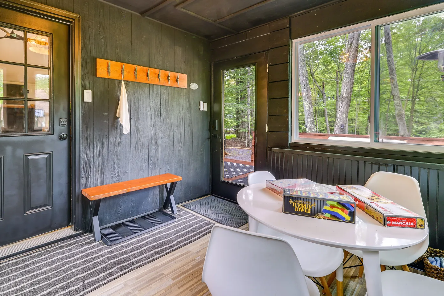 Enclosed porch entryway featuring dark wood paneled walls, a small dining table with board games, a bench, and a coat rack.