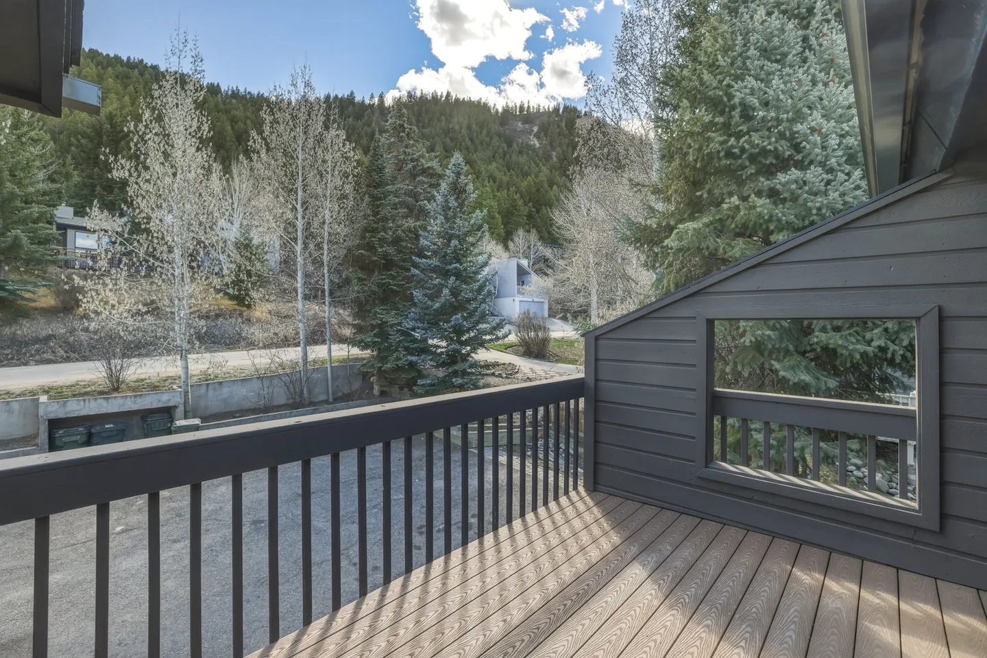 Outdoor balcony with dark wood railing and decking overlooking trees and a forested hillside.