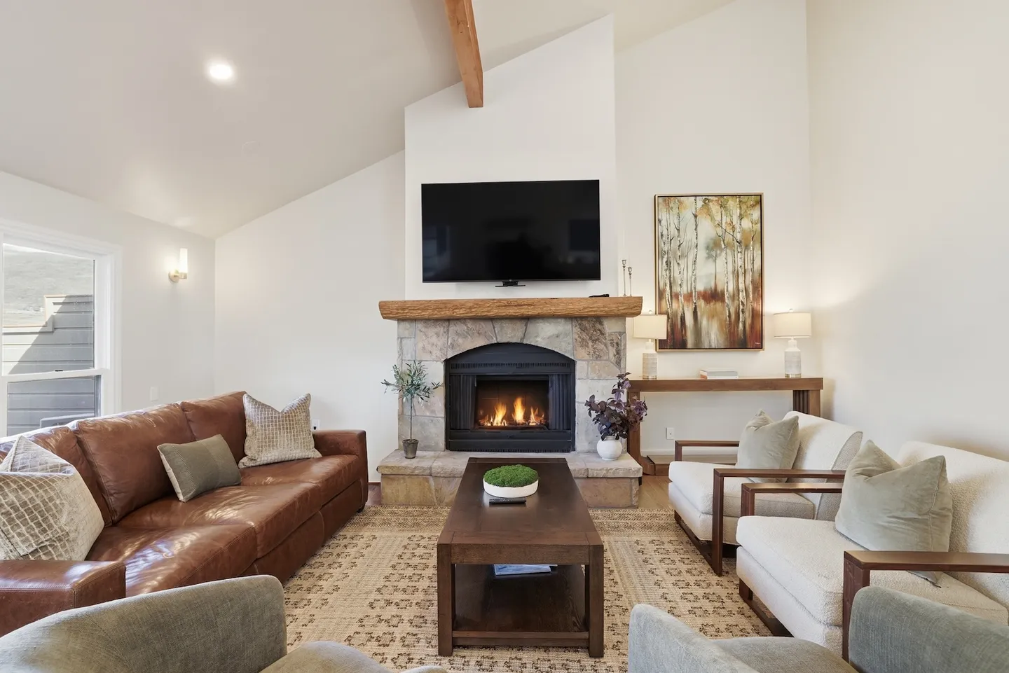Living room with a stone fireplace, mounted TV, leather sofa, armchairs, and vaulted ceilings.