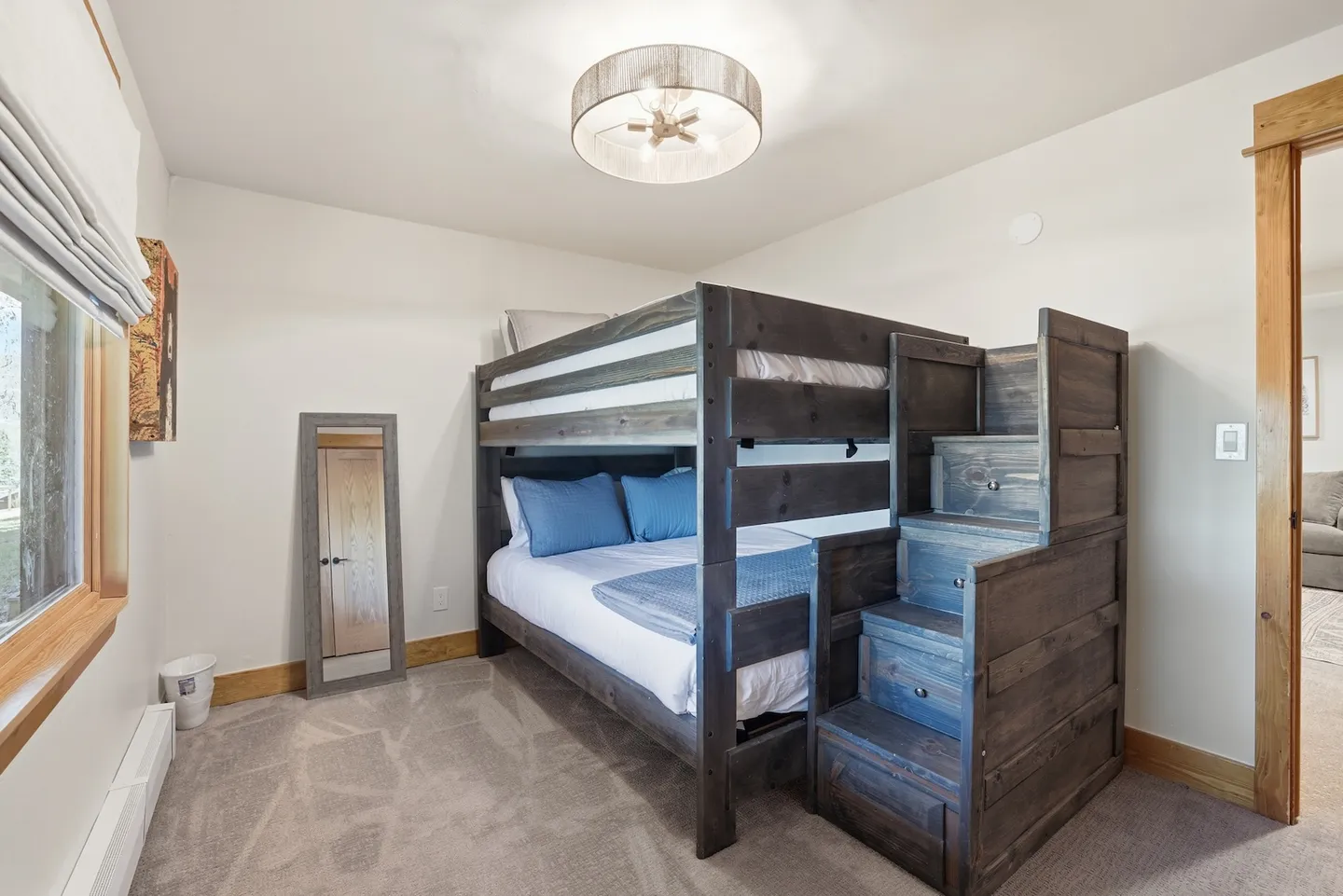 Bedroom with a dark wood bunk bed featuring integrated step drawers, carpeted flooring, and a full-length floor mirror.