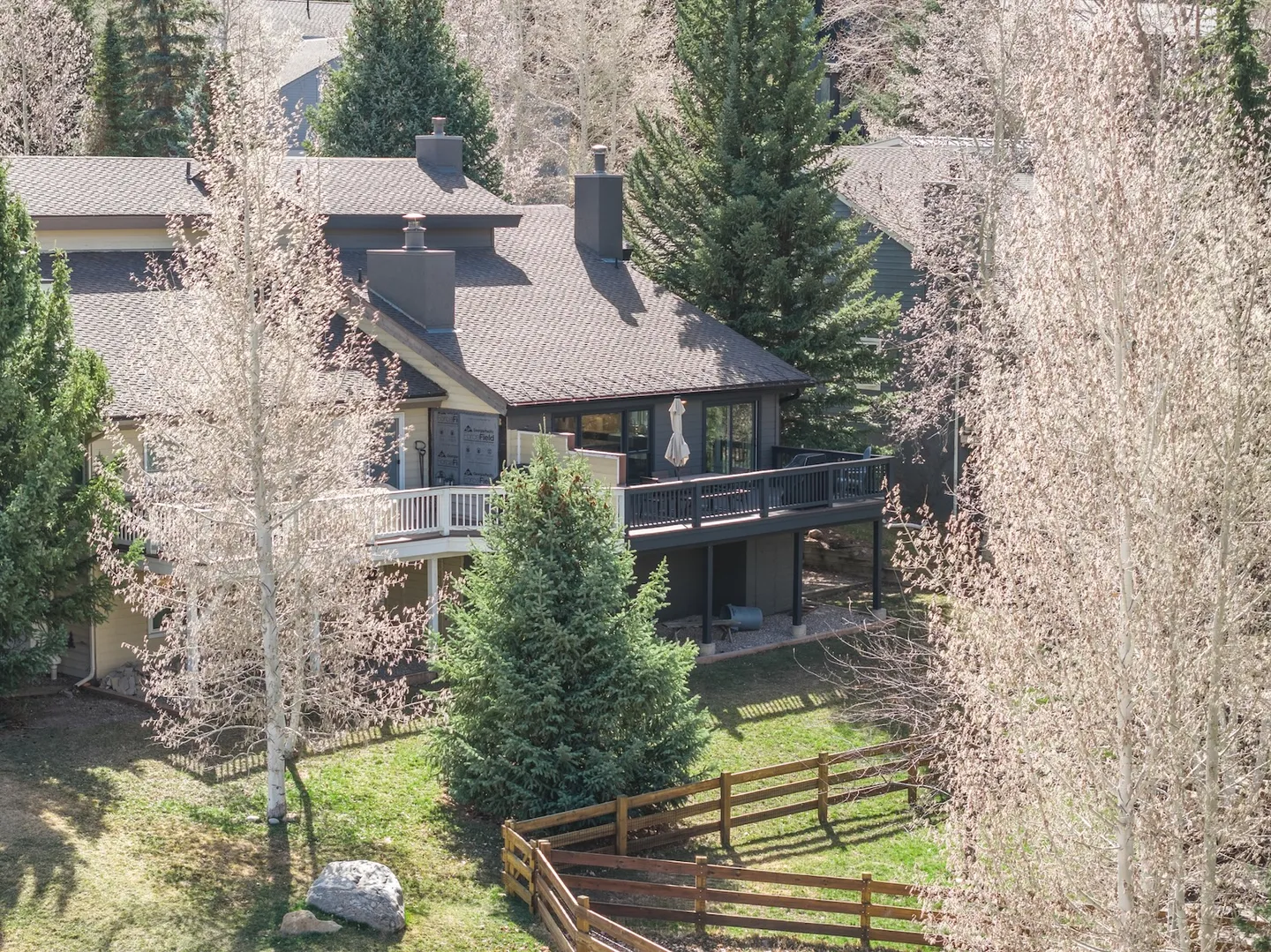 Elevated view of a multi-story home with upper-level decks framed by tall trees and a wooden rail fence.