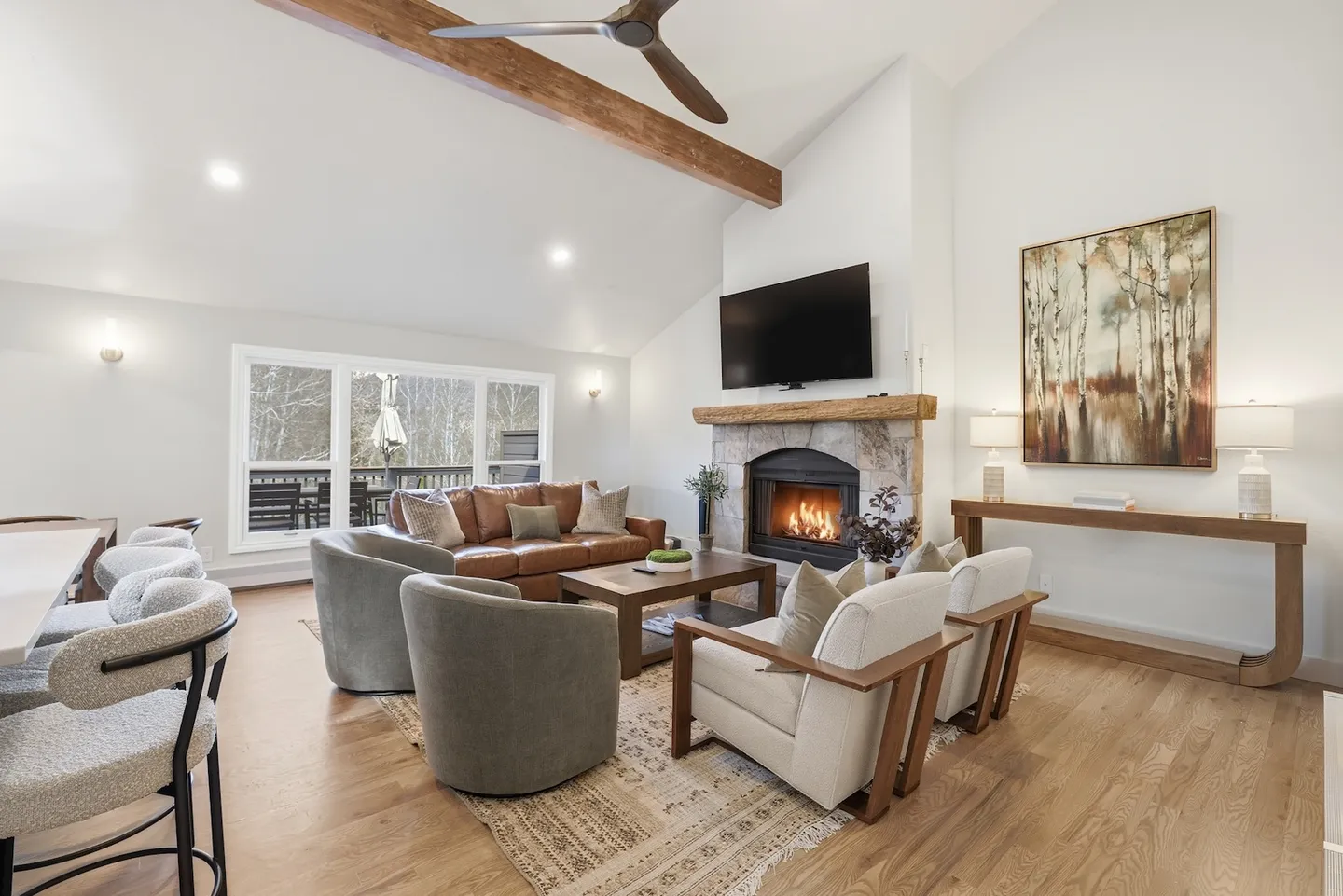 Bright living room featuring vaulted ceilings, an exposed wooden beam, a stone fireplace, and a mounted TV above the mantel.