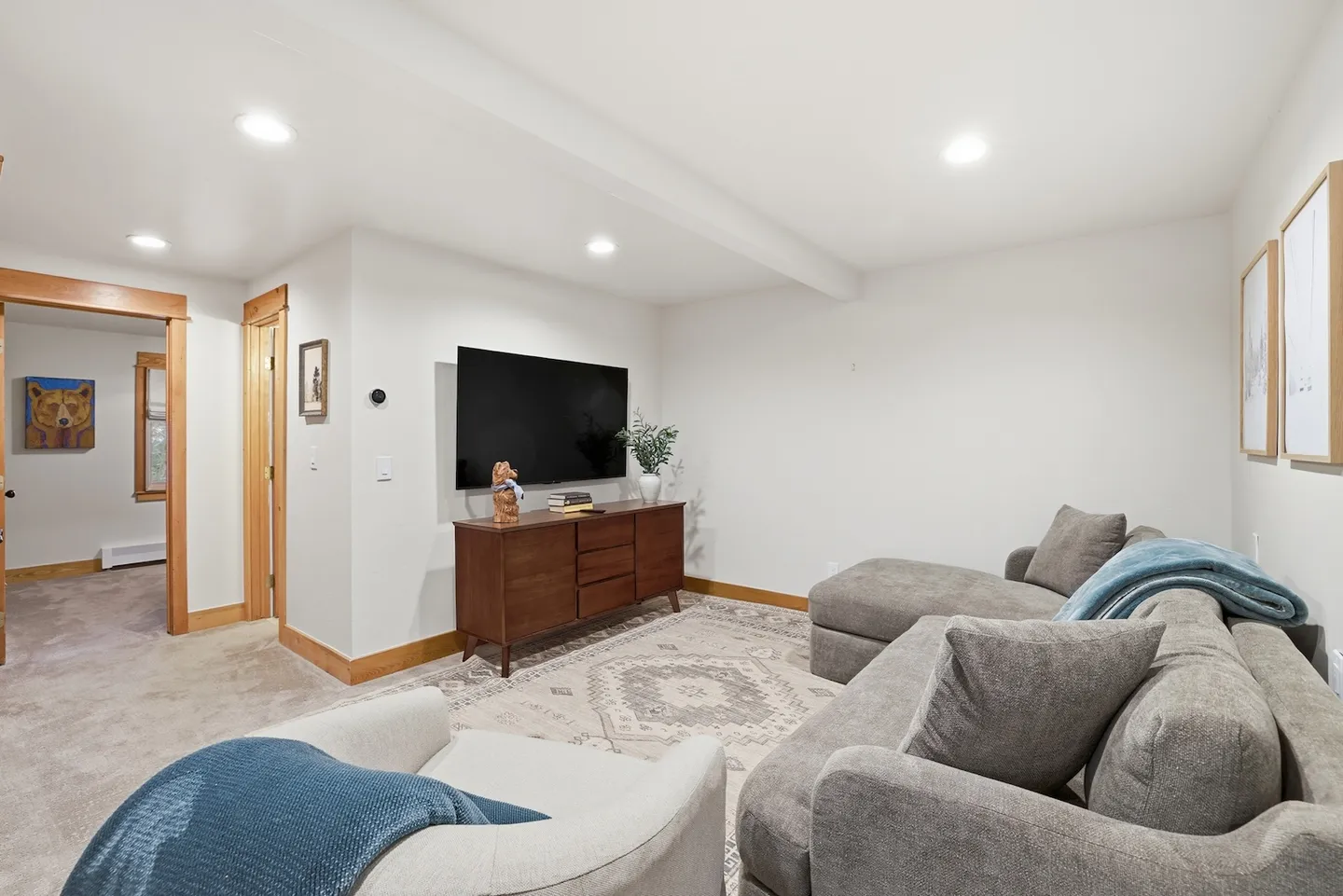 Living room with plush grey sectional sofa, an armchair, a wall-mounted TV over a wooden media console, and carpeted floors.