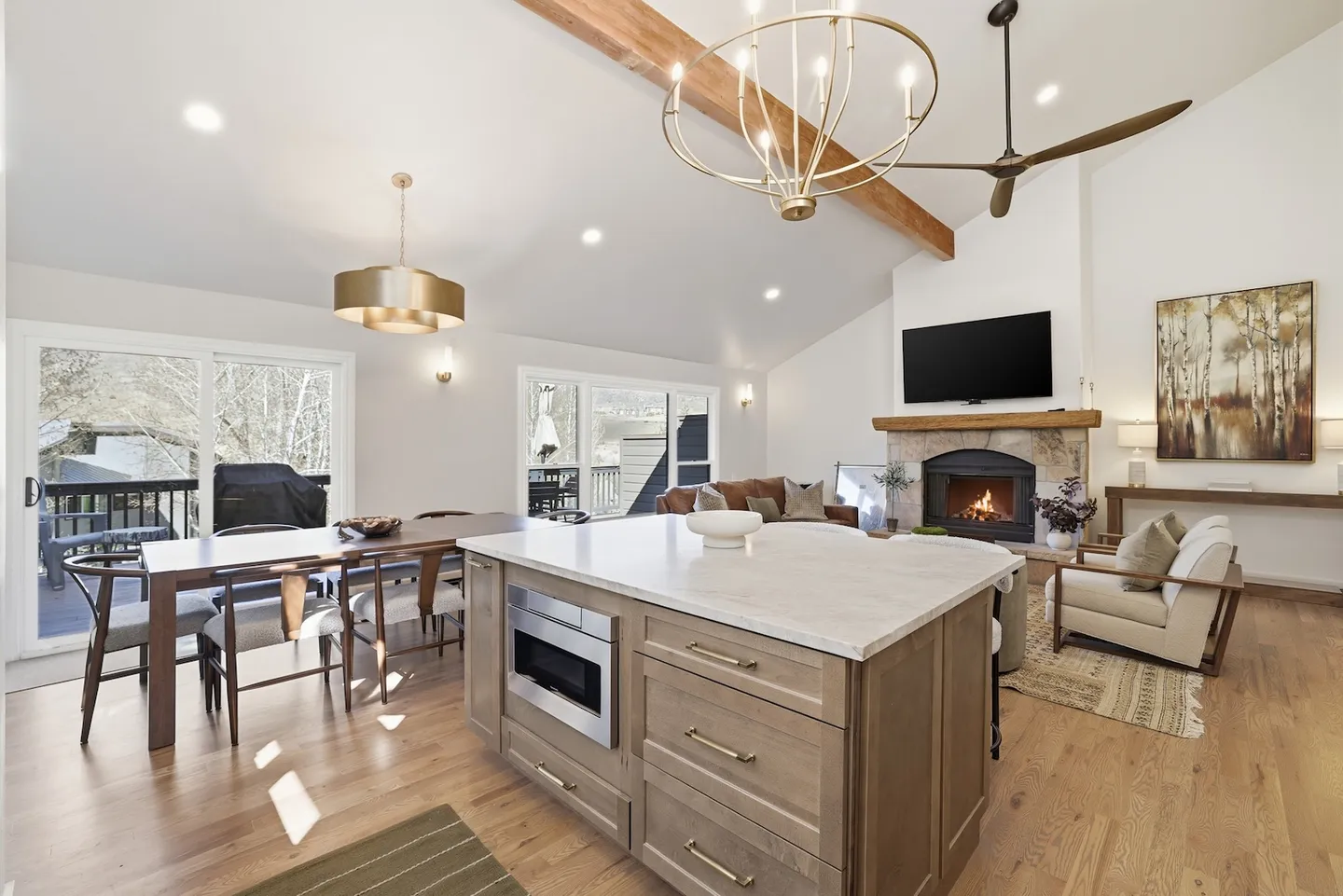 Open-concept living and dining area with a kitchen island in the foreground, dining table, and living room with a fireplace.