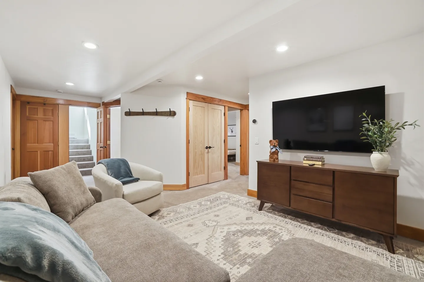Lower level living room with sofa, armchair, area rug, wall-mounted television, and media console.