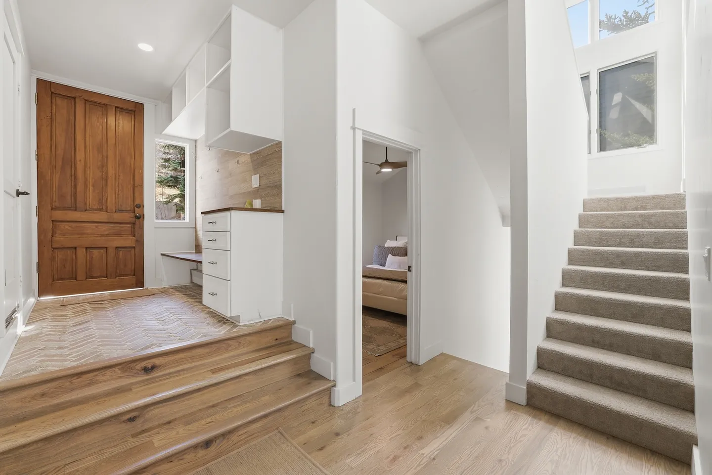 Entryway with a wooden front door, parquet tile floor, built-in storage cabinets, wood steps, and a carpeted staircase.