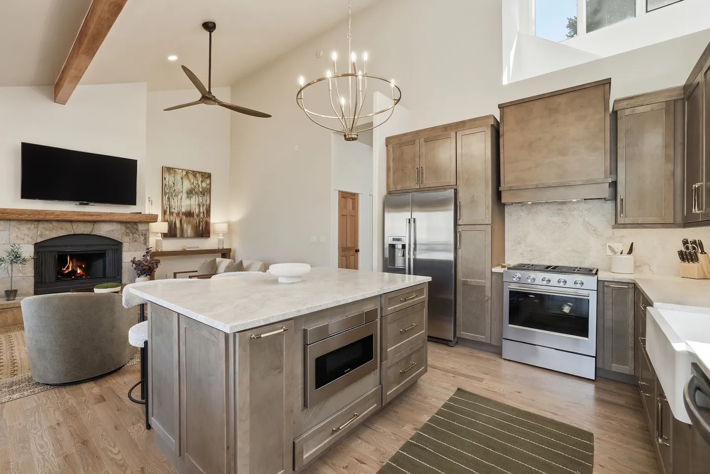 Open concept kitchen and living room featuring a central island with built-in microwave, stainless steel appliances, and a living area with a fireplace and television.
