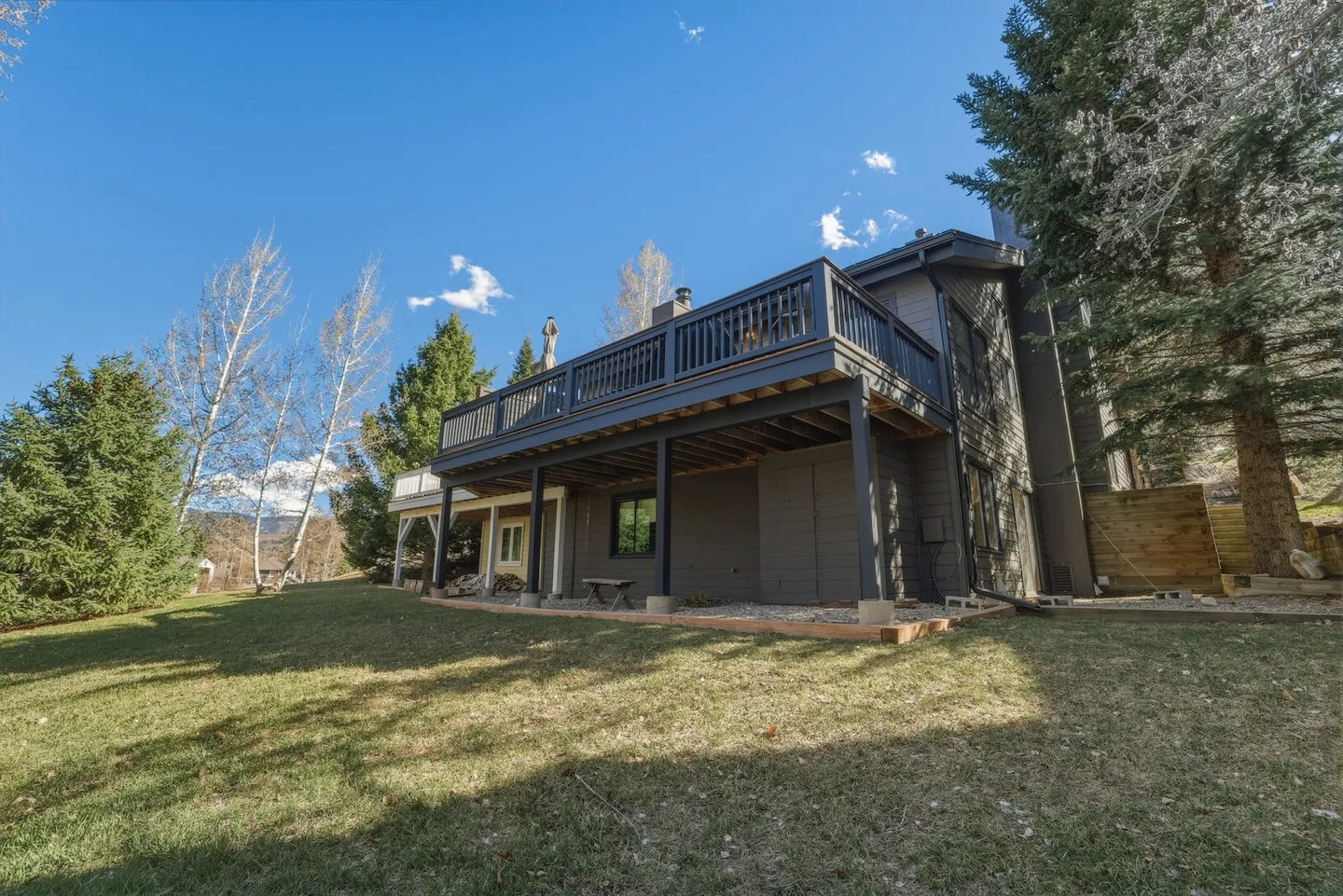 Exterior rear view of a two-story home with a large upper-level deck and a grassy backyard.
