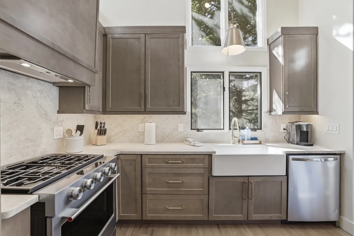 A bright kitchen corner featuring wood cabinetry, stainless steel appliances, a white apron-front sink, and windows letting in daylight.