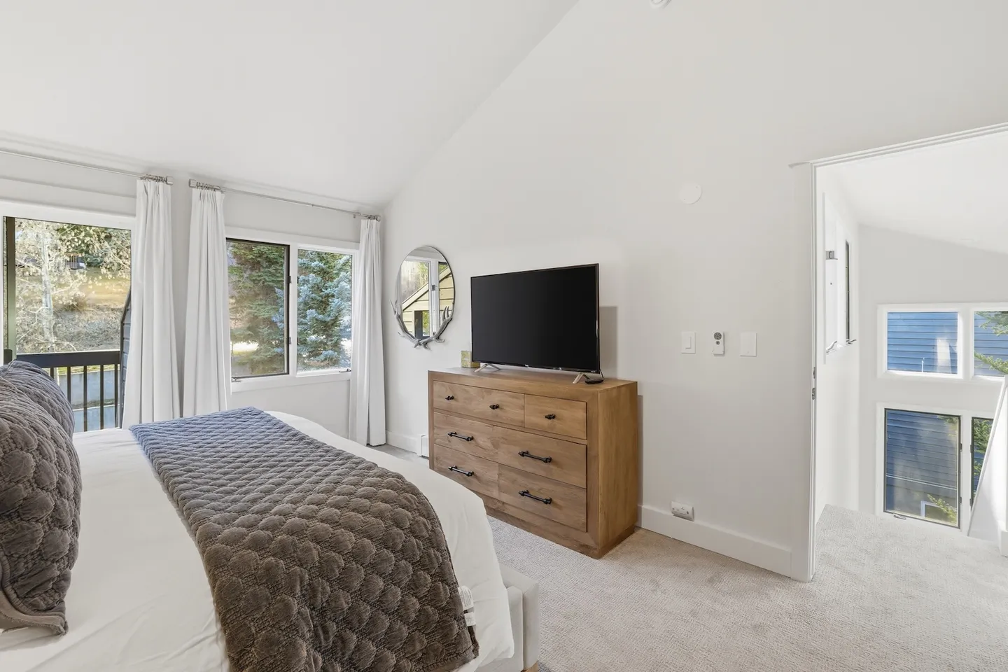 Bedroom with vaulted ceiling, carpeted floor, bed with brown quilt, wooden dresser with a TV on top, and sliding glass doors.