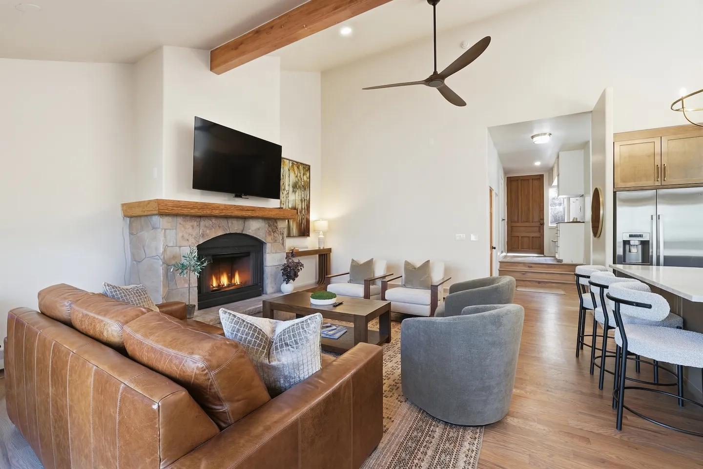 Living room with vaulted ceiling, stone fireplace, leather sofa, and modern armchairs adjacent to the kitchen bar counter.