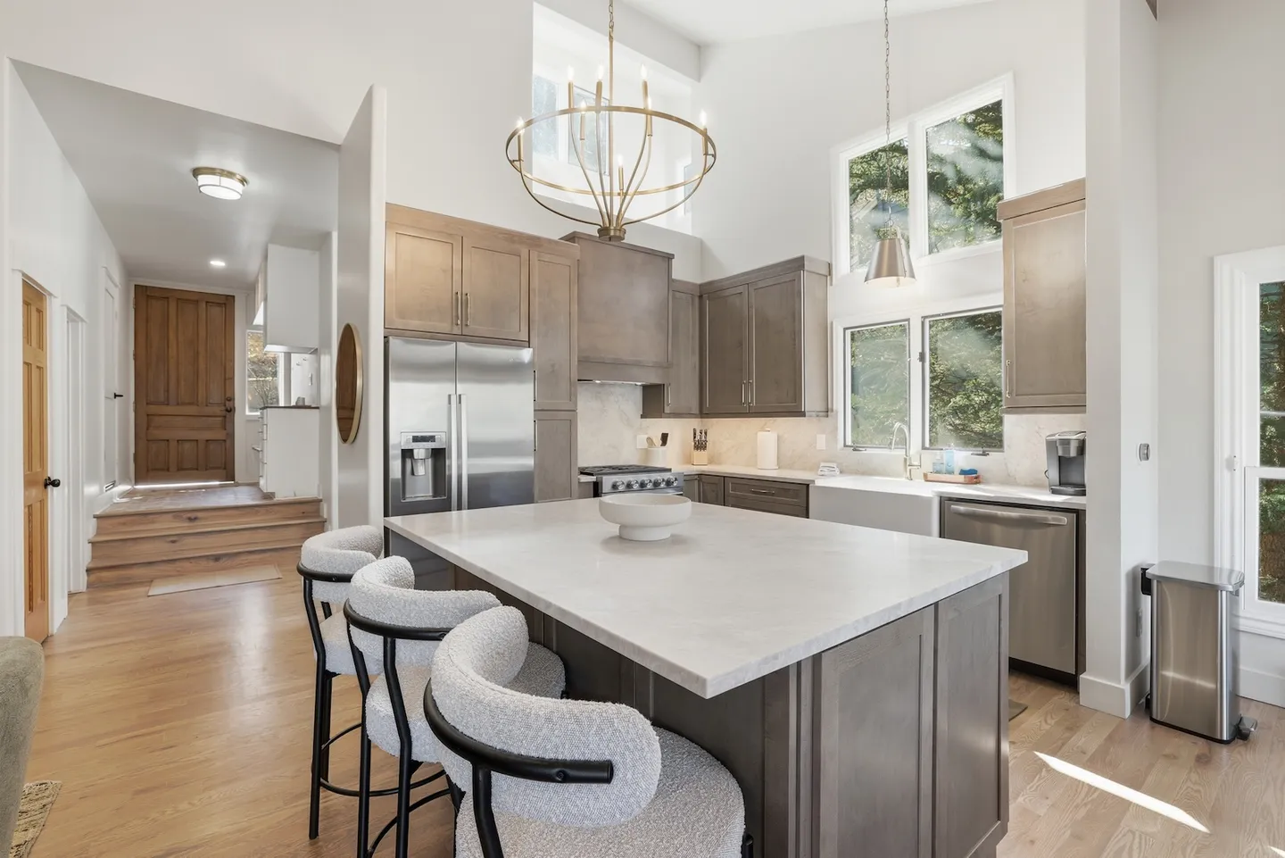 Kitchen with large center island, upholstered bar stools, stainless steel appliances, and high ceilings.