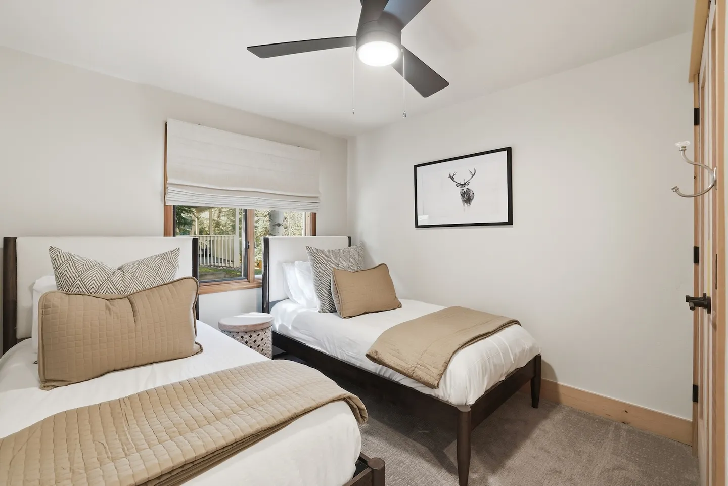 Bedroom with two twin beds dressed in white and tan linens, carpeted floor, ceiling fan, and window.
