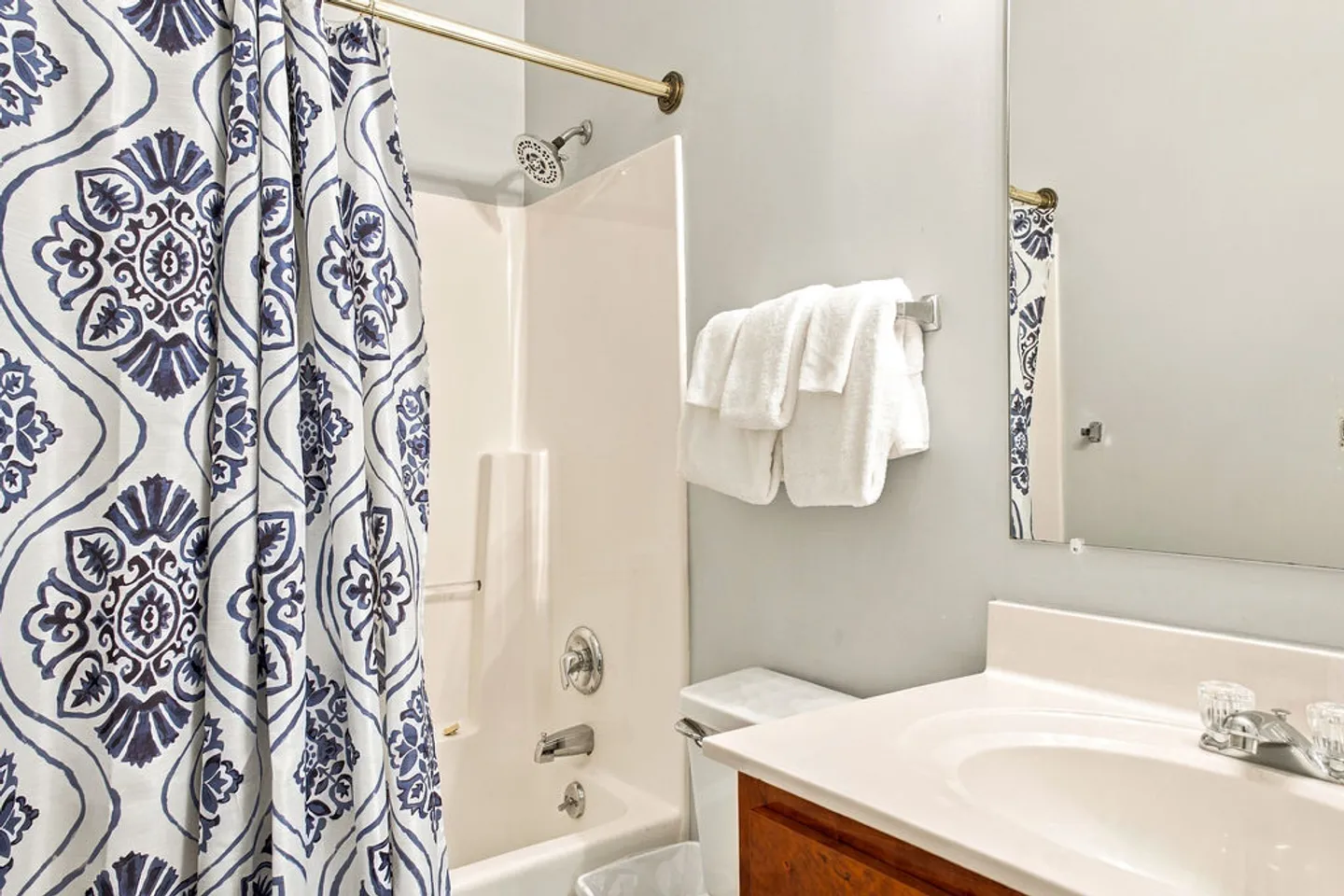 Bathroom with a bathtub and shower combination, blue patterned shower curtain, toilet, towel bar with white towels, and a vanity sink.