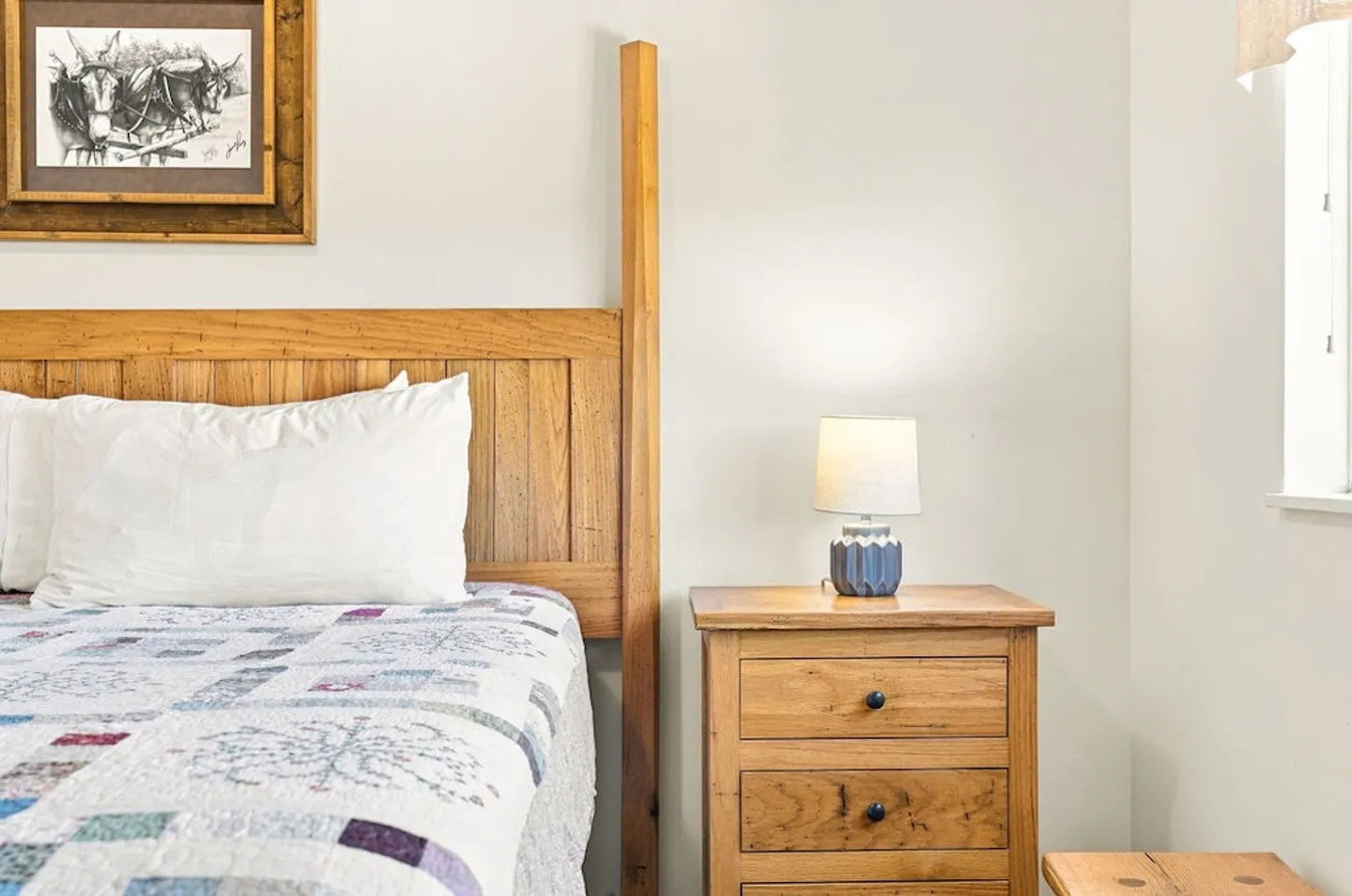 Bedroom detail showing a wooden headboard, a bed with a patchwork quilt, and a wooden nightstand with a lamp.