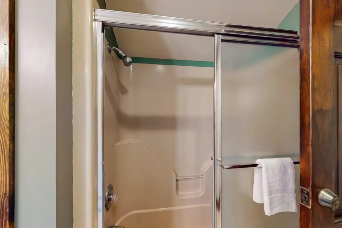 Bathroom shower with sliding frosted glass doors and silver trim, showing showerhead and molded tub-shower surround.