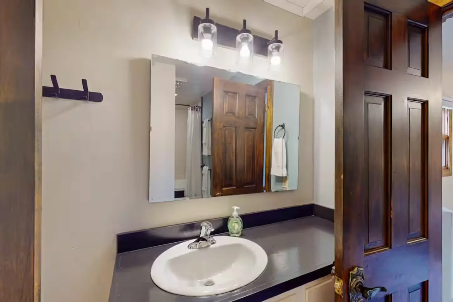 Bathroom vanity with an oval sink, dark countertop, rectangular mirror, and three-bulb vanity light.