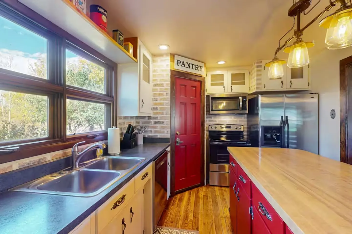 Kitchen interior featuring a red pantry door, butcher block island, stainless steel appliances, and a window above the double sink.