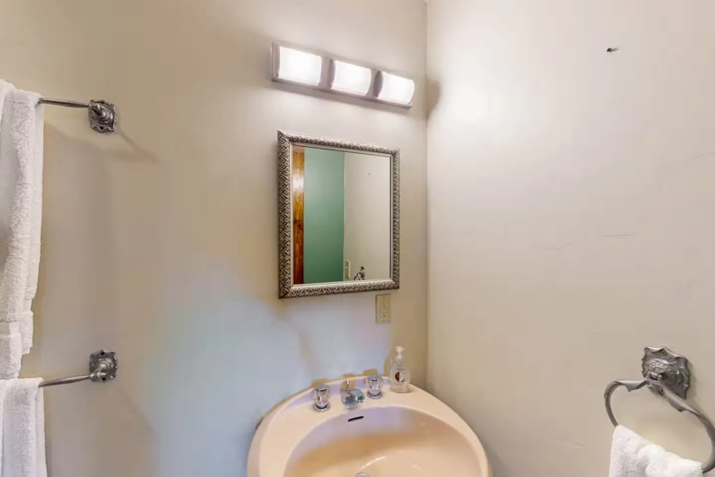 Bathroom vanity area featuring a peach-toned sink, framed mirror, wall light fixture, and towel racks.