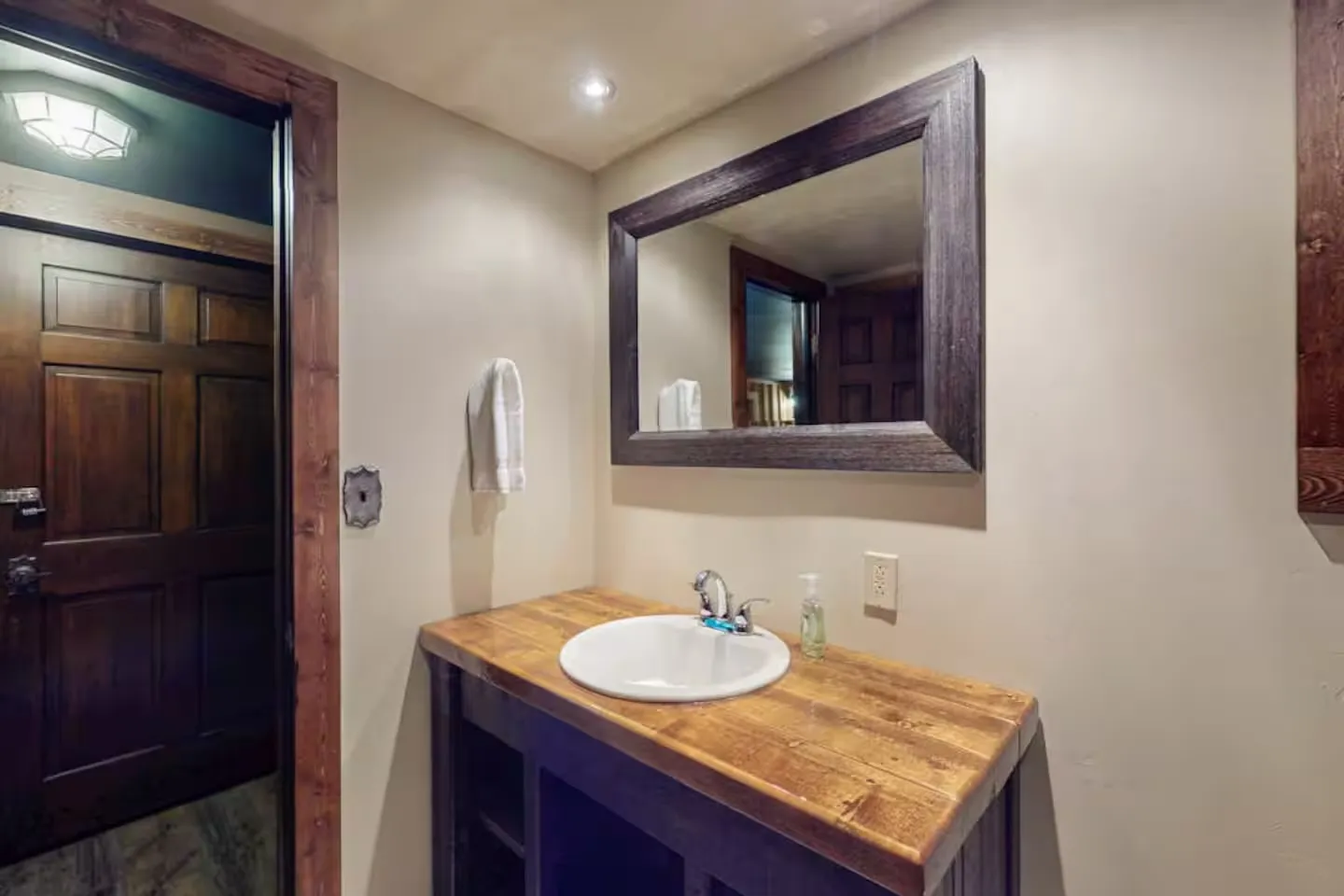 Bathroom vanity with a wood countertop, drop-in sink, and rustic wood-framed mirror.
