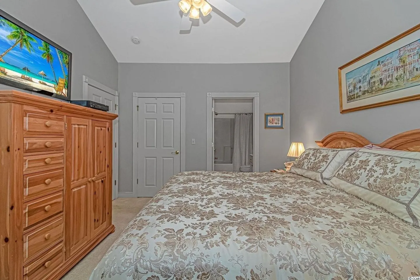 Bedroom featuring a patterned bedspread, wooden armoire with a television, and an en-suite bathroom doorway.