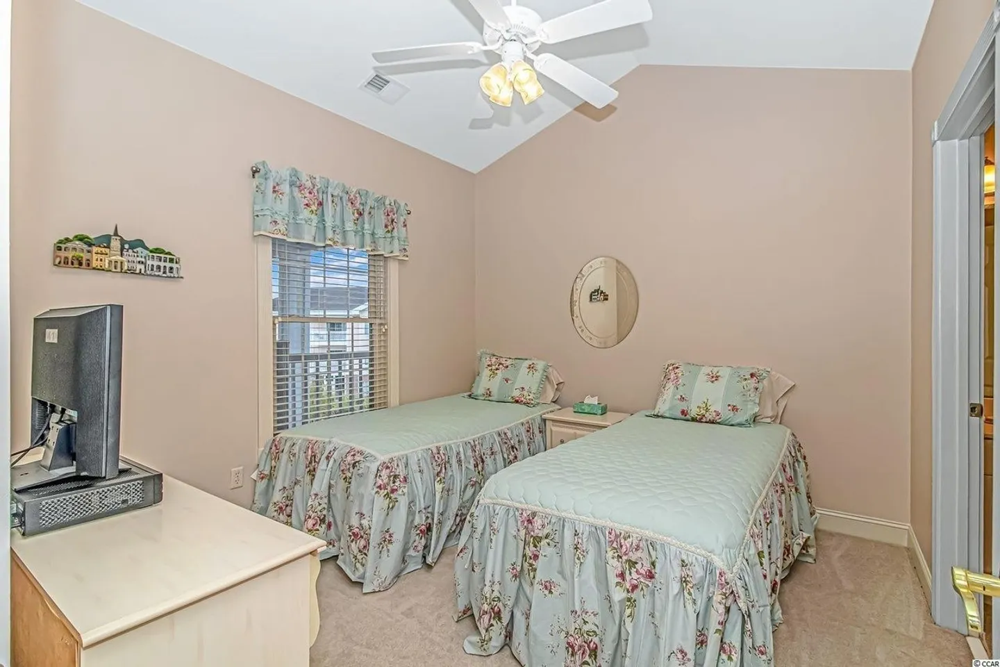 Bedroom with two twin beds dressed in floral dust ruffles and mint green quilts, carpeted flooring, a ceiling fan, and a television on a dresser.