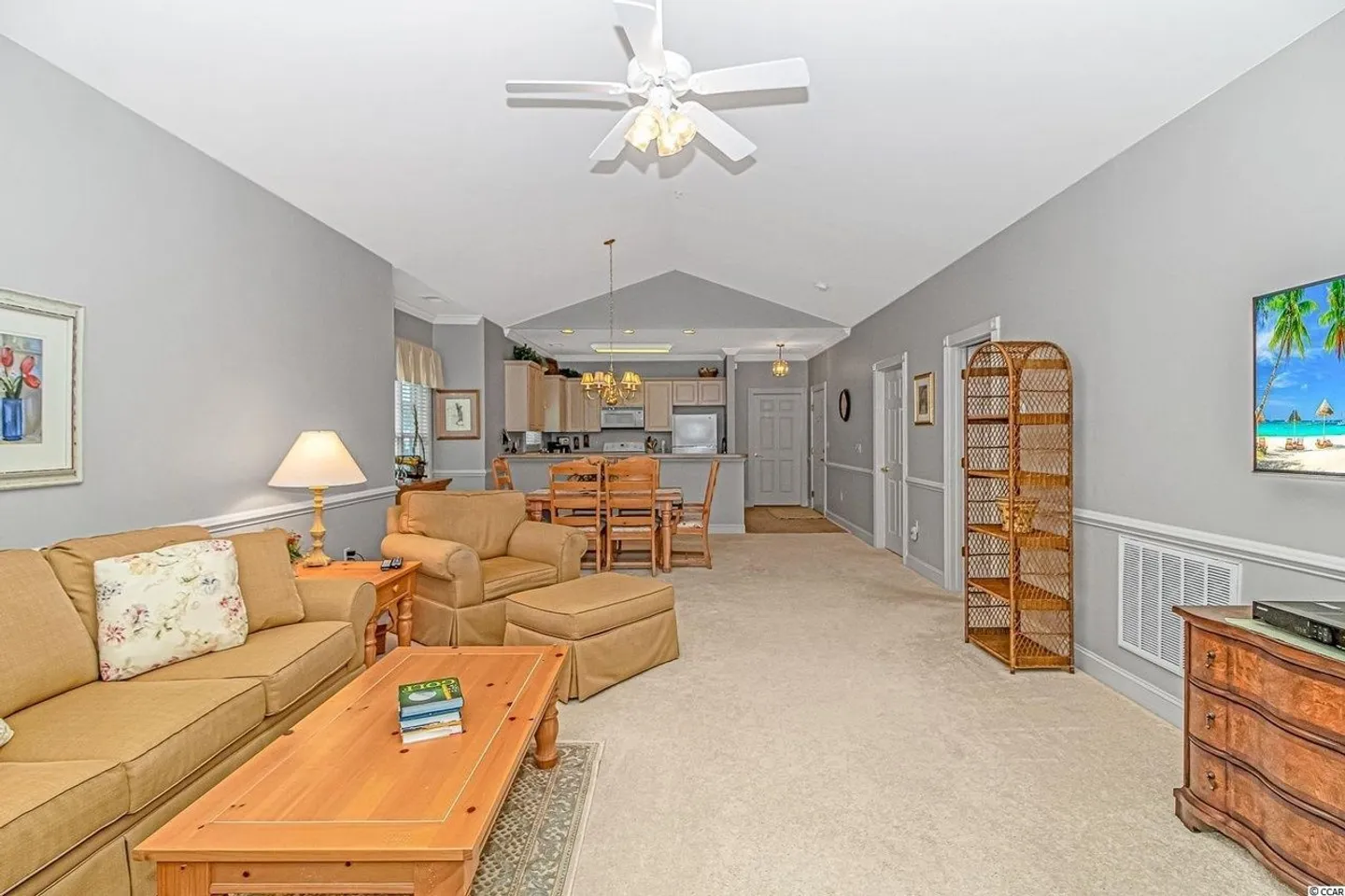 Open-concept living room with carpet, a sofa, armchair, coffee table, and an open view into the dining area and kitchen.