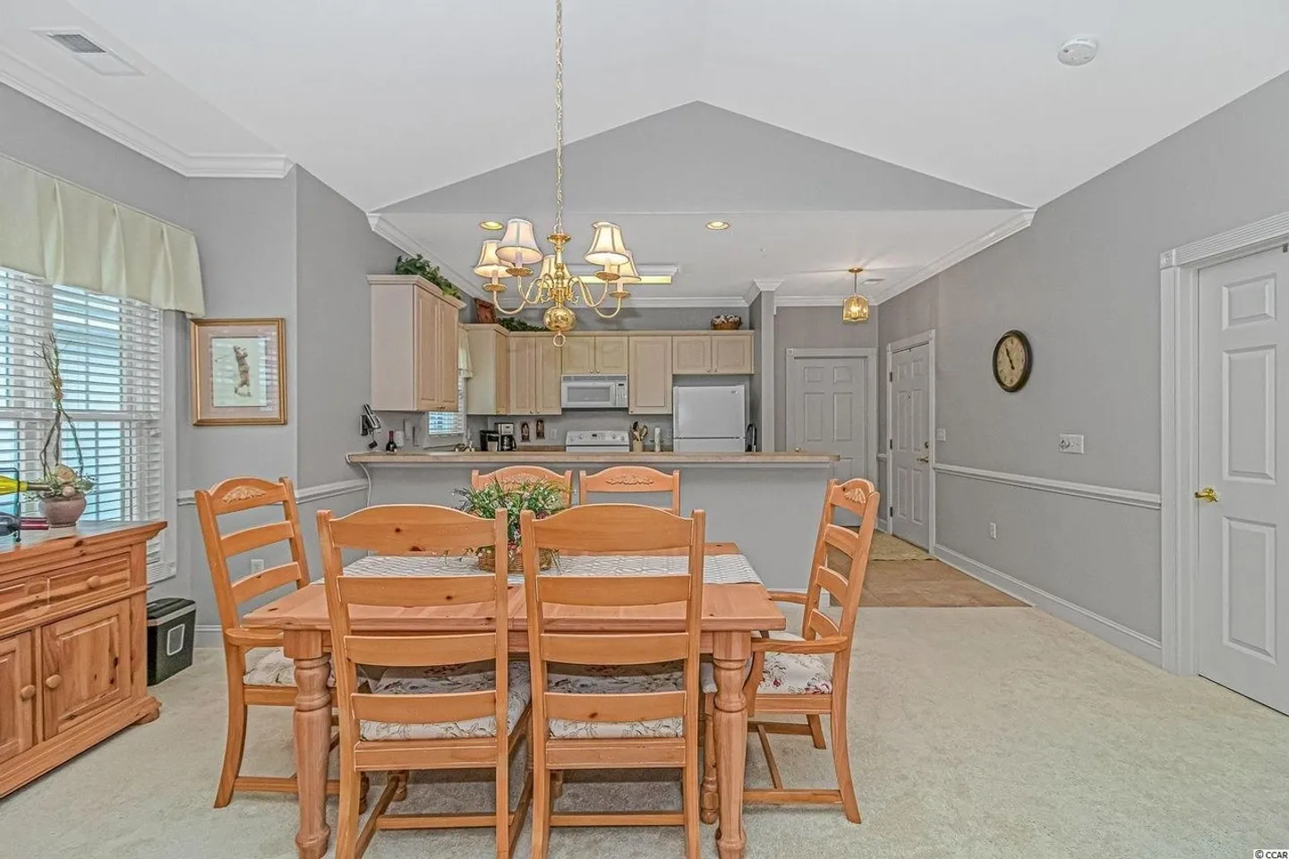 Dining area with a wooden table and chairs in the foreground opening directly into a kitchen.