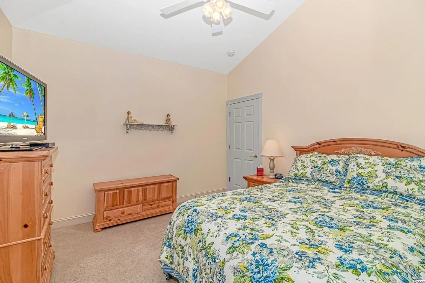 Bedroom featuring a bed with a floral comforter, light wood furniture, a television on a tall dresser, and vaulted ceilings.