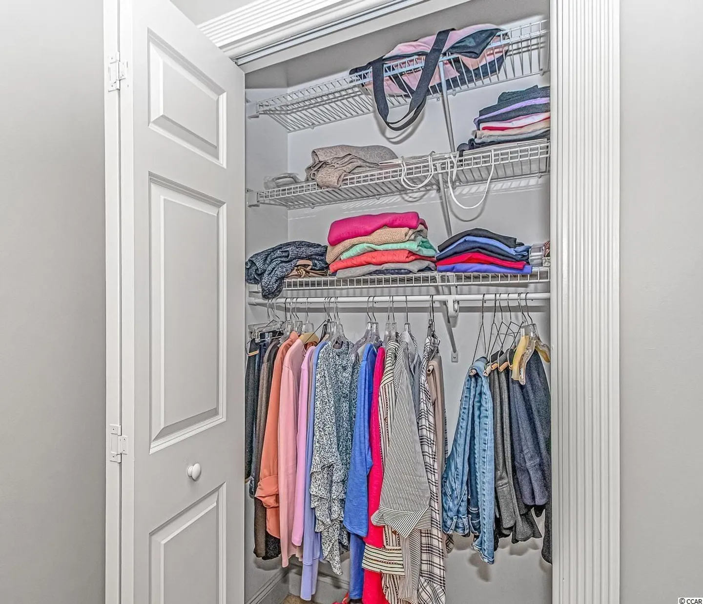 Open closet with white wire shelving holding folded and hanging clothes.