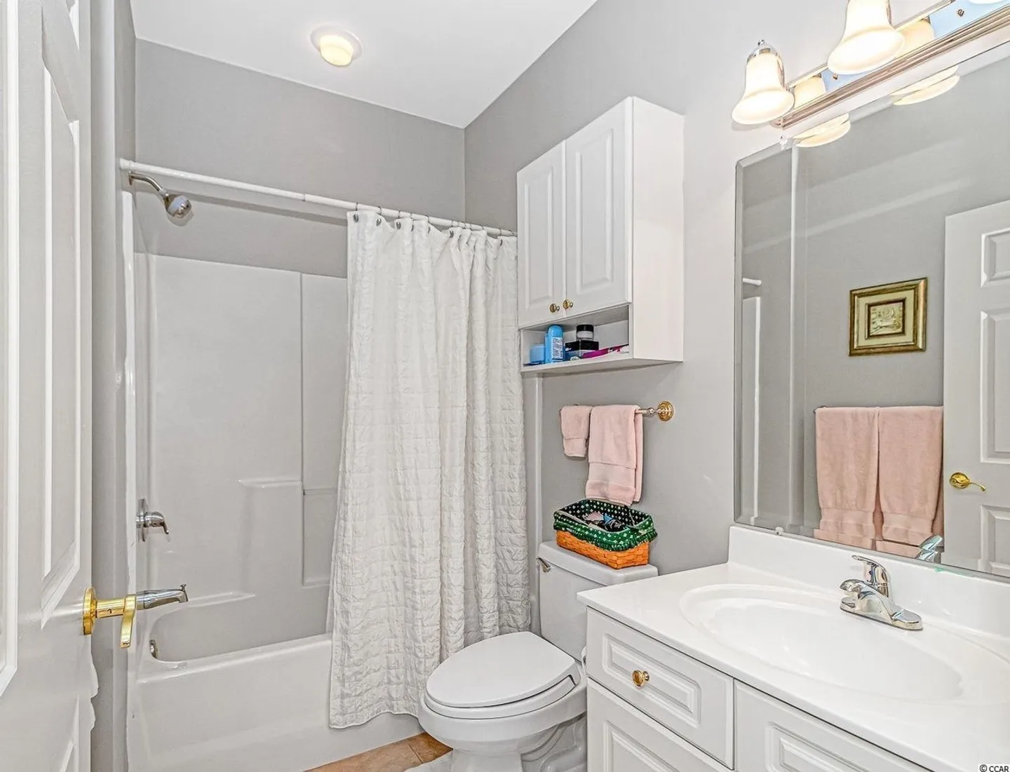 Bathroom with a white vanity, toilet, wall cabinet, and a shower-tub combination with a white curtain.