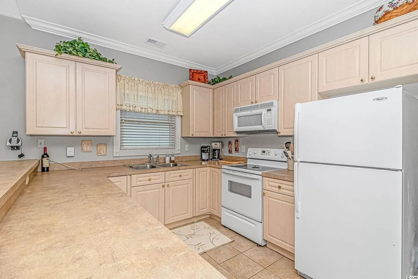 Kitchen with light-colored wood cabinets, white appliances, beige countertops, and tile flooring.